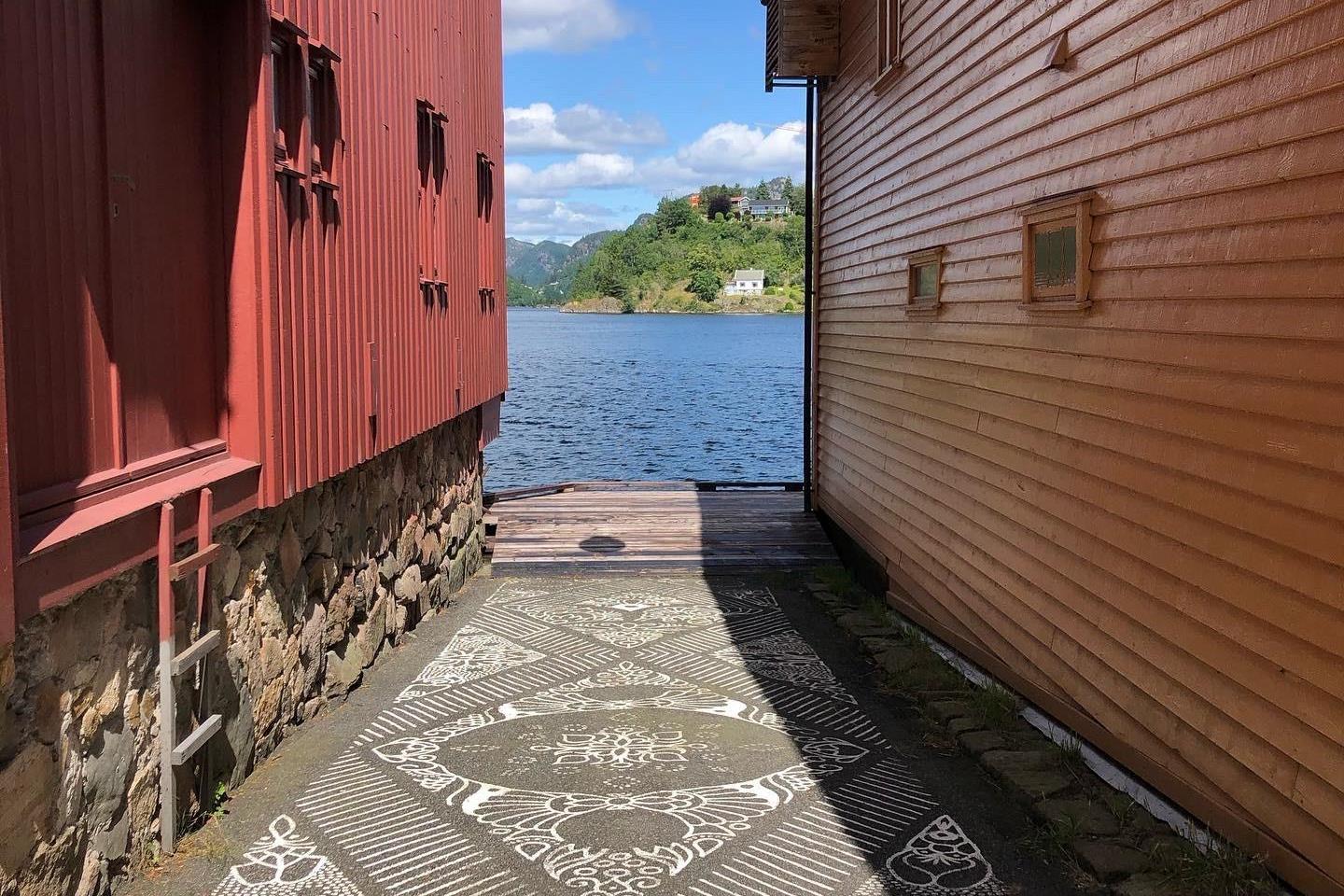 Blå, himmel, hav og to sjøboder. Gatekunst på bakken i forgrunn.