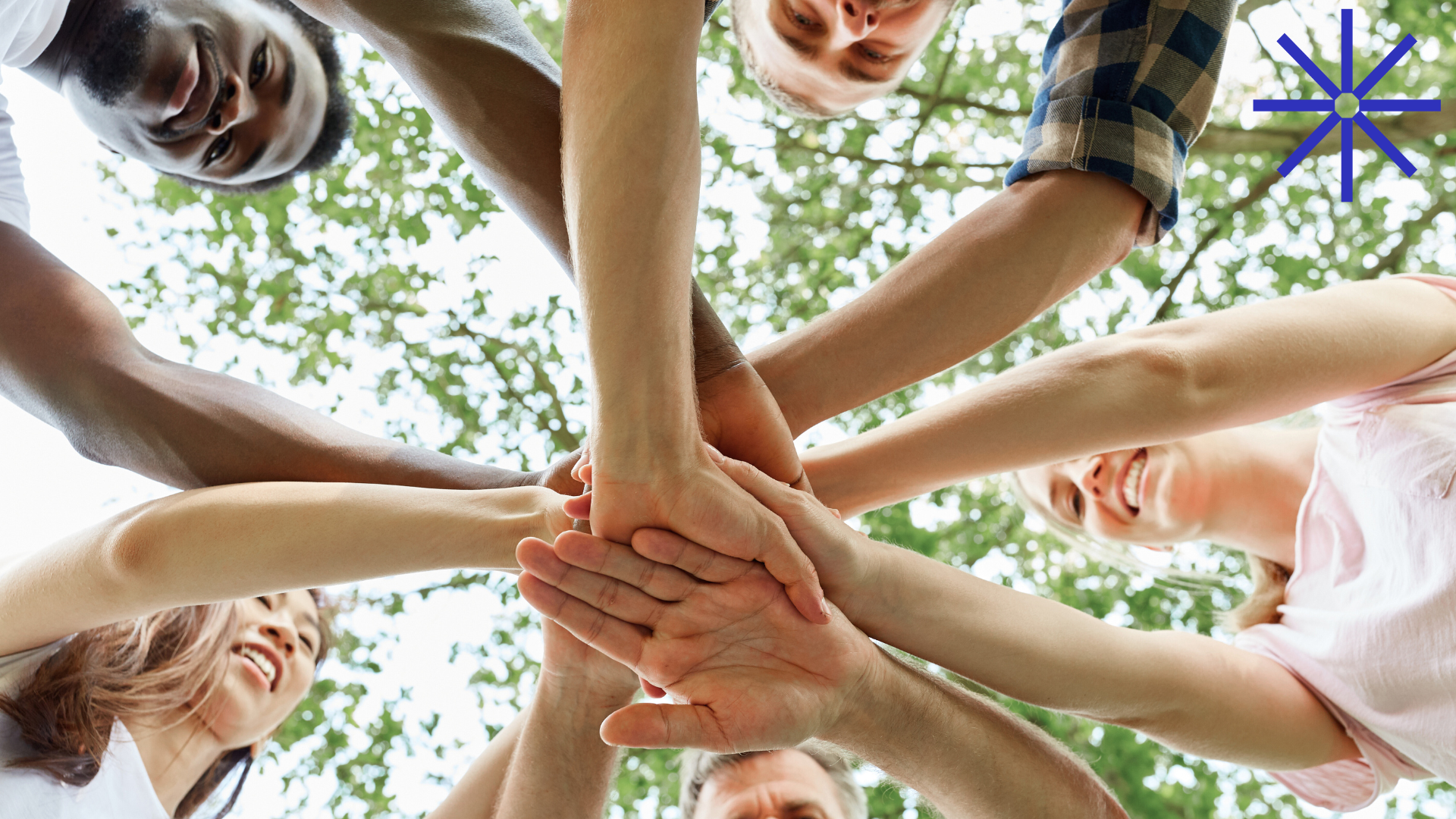 Foto av flere voksne personer som holder hendene samlet i midten av en sirkel.
