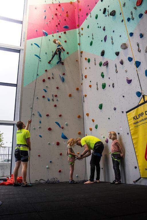 Et barn klatrer mens klatreverten sikrer. En annen klatrevert seler på et annen barn. - Klikk for stort bilde