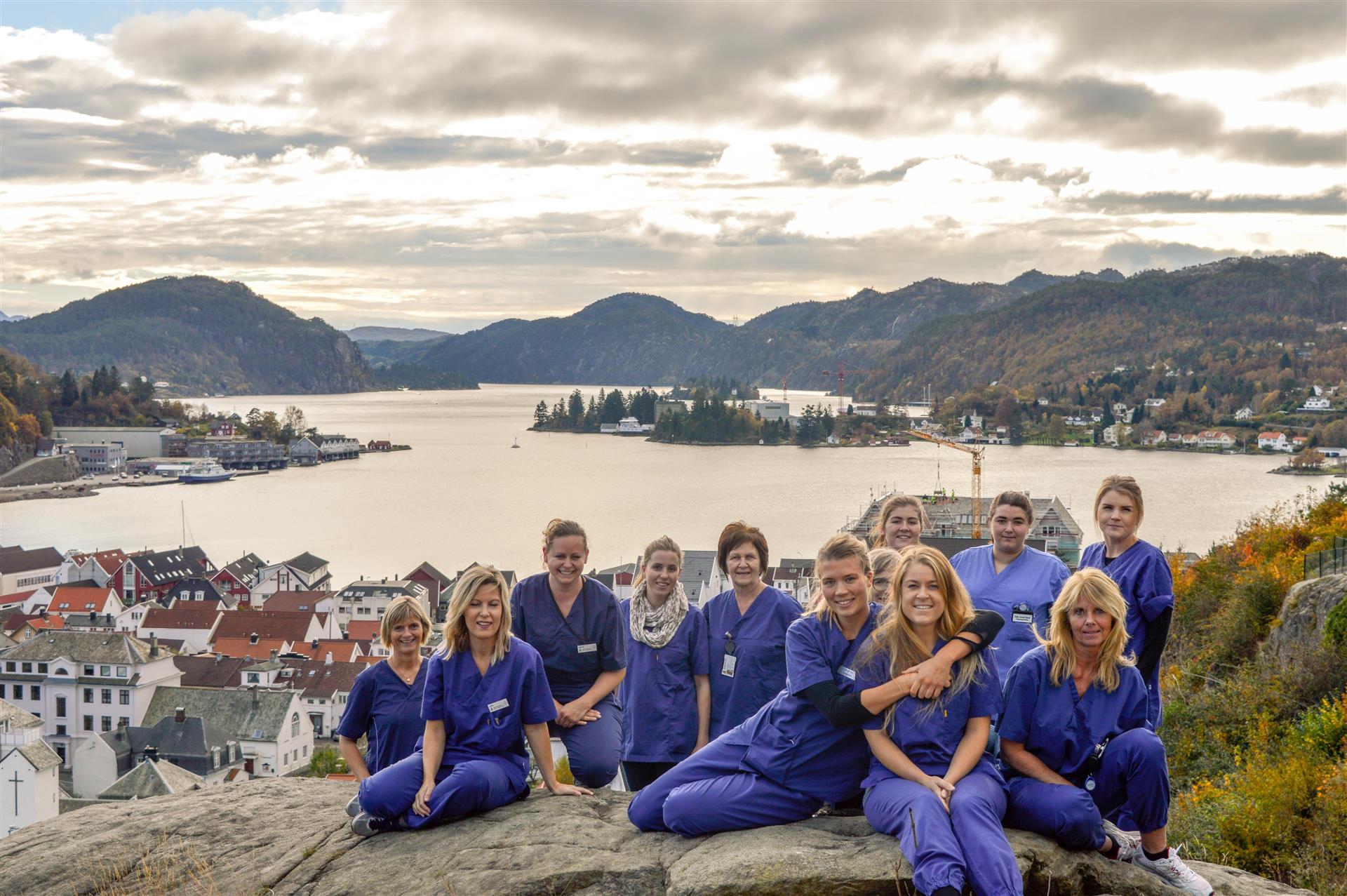 Mennesker i sykepleieruniform, med sjø og by som bakgrunn.