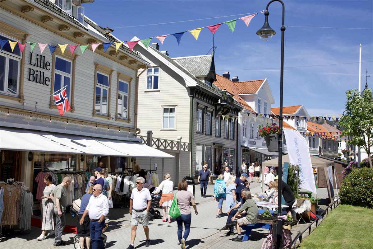 Mennesker, bygg og blå himmel i Flekkefjord sentrum. - Klikk for stort bilde