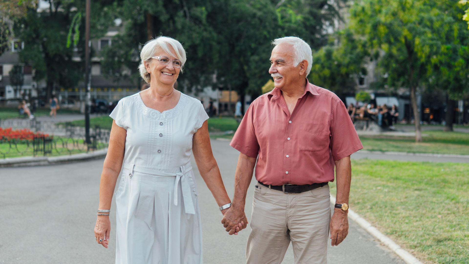 En eldre dame med hvitt hår går hånd i hånd med en eldre mann med hvitt hår, de ser lykkelige ut