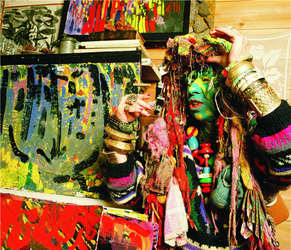 Tatjana Lars Kristian Gulbrandsen ikledd flere lag med klær, smykker og armbånd. Ansiktet er malt i ulike farger. 